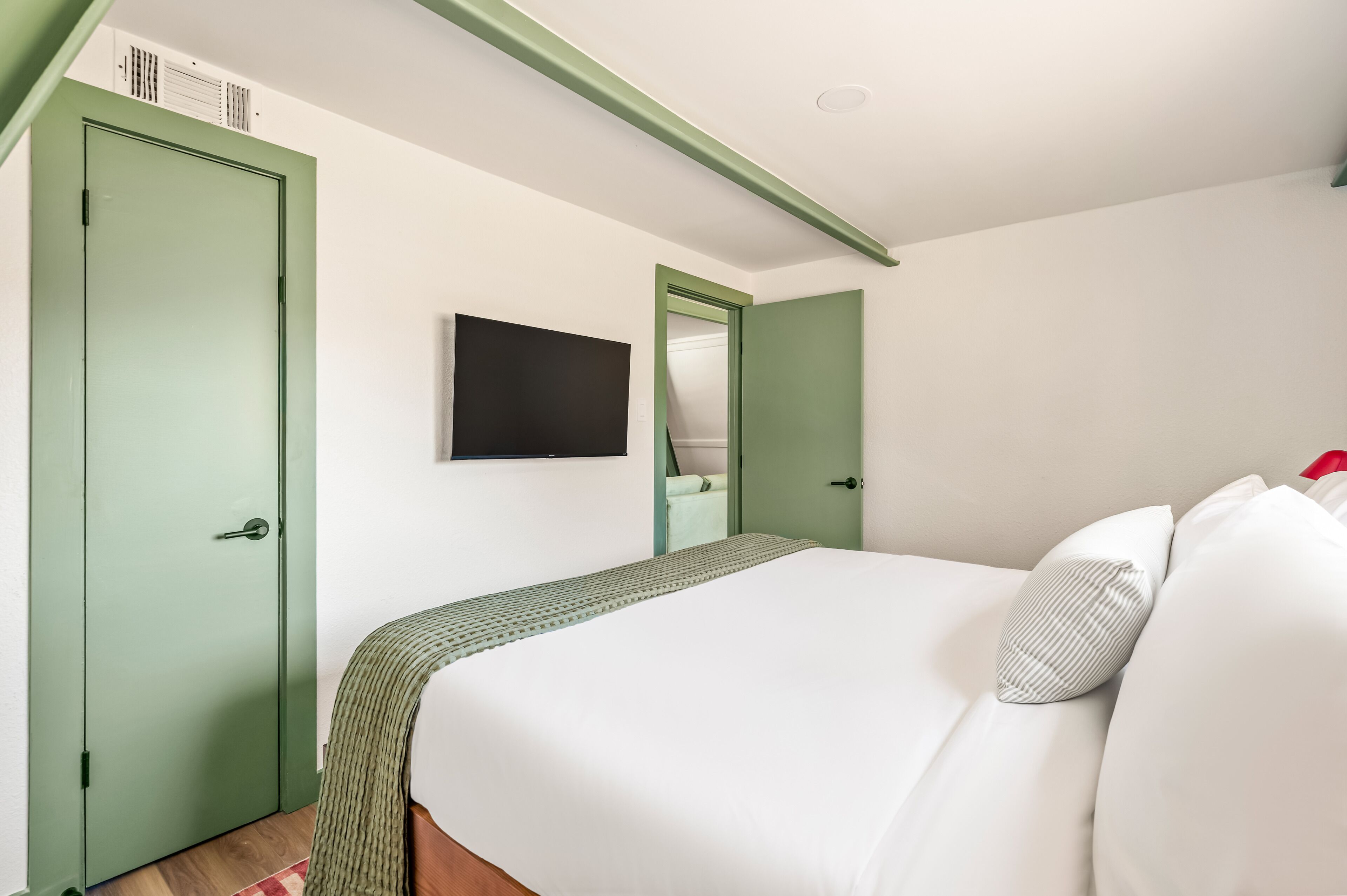 A bedroom with a bed, a green door, a television, and a mirror.
