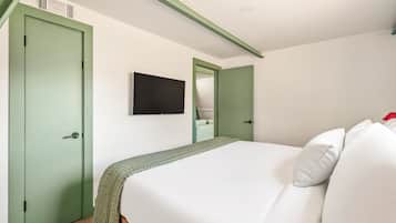 A bedroom with a bed, a green door, a television, and a mirror.