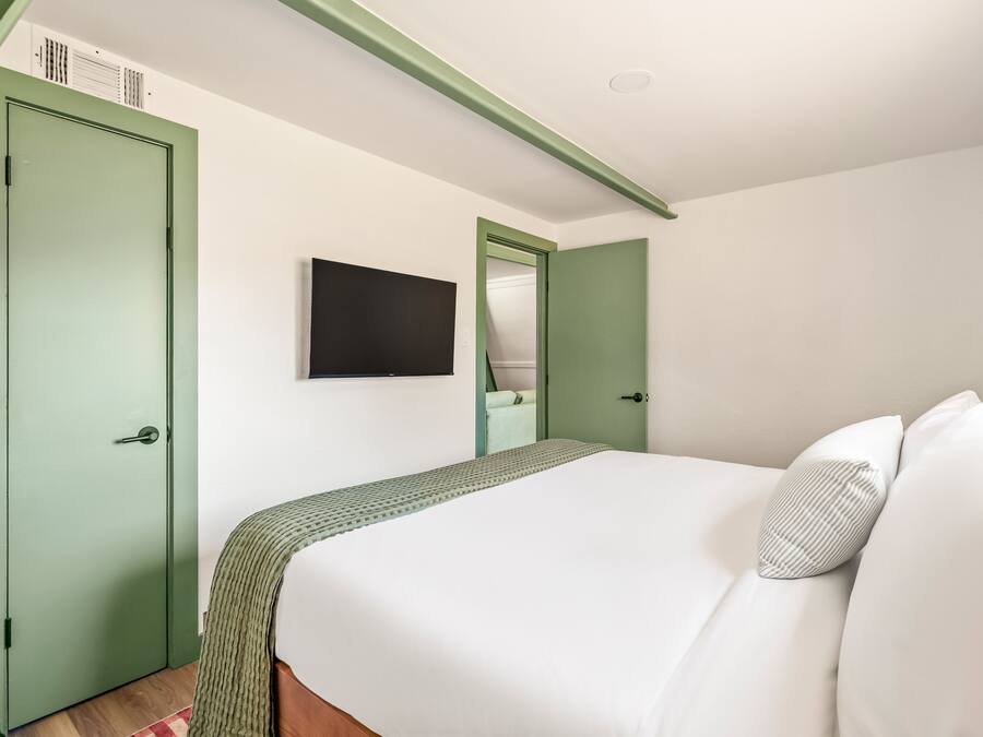 A bedroom with a bed, a green door, a television, and a mirror.