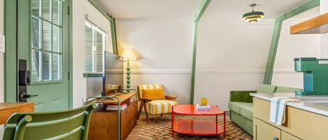 Una habitación compacta y bien iluminada, con una puerta verde, una mesa de madera, un pequeño café rojo, un sillón a rayas y un sofá verde.