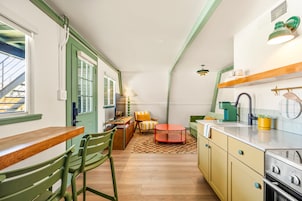 Uma cozinha compacta com área de refeições, apresentando uma mesa de madeira, cadeiras verdes, uma mesa vermelha e um armário amarelo.