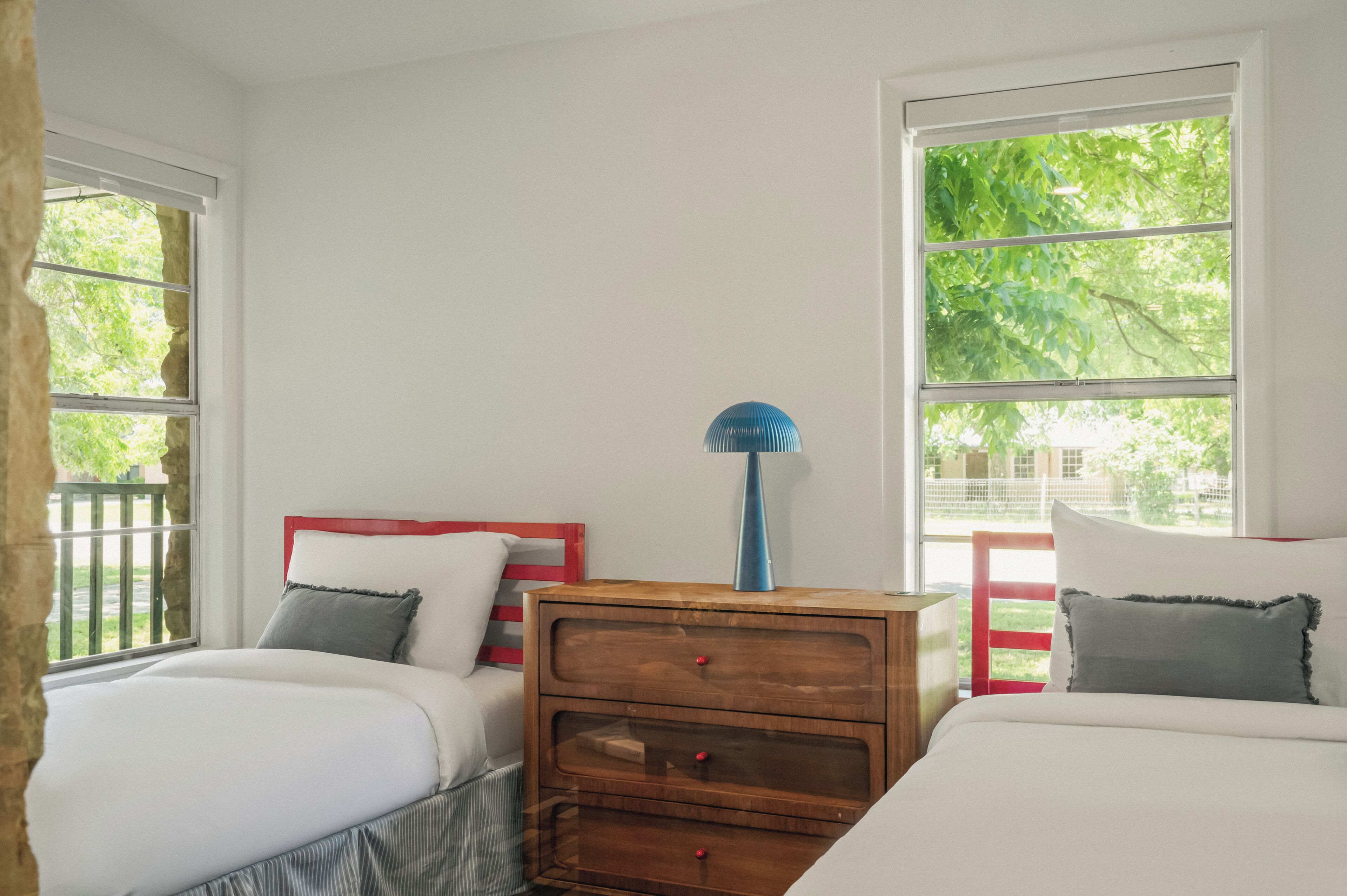 A bedroom with two beds, a wooden nightstand, and large windows.