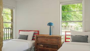 A bedroom with two beds, a wooden nightstand, and large windows.