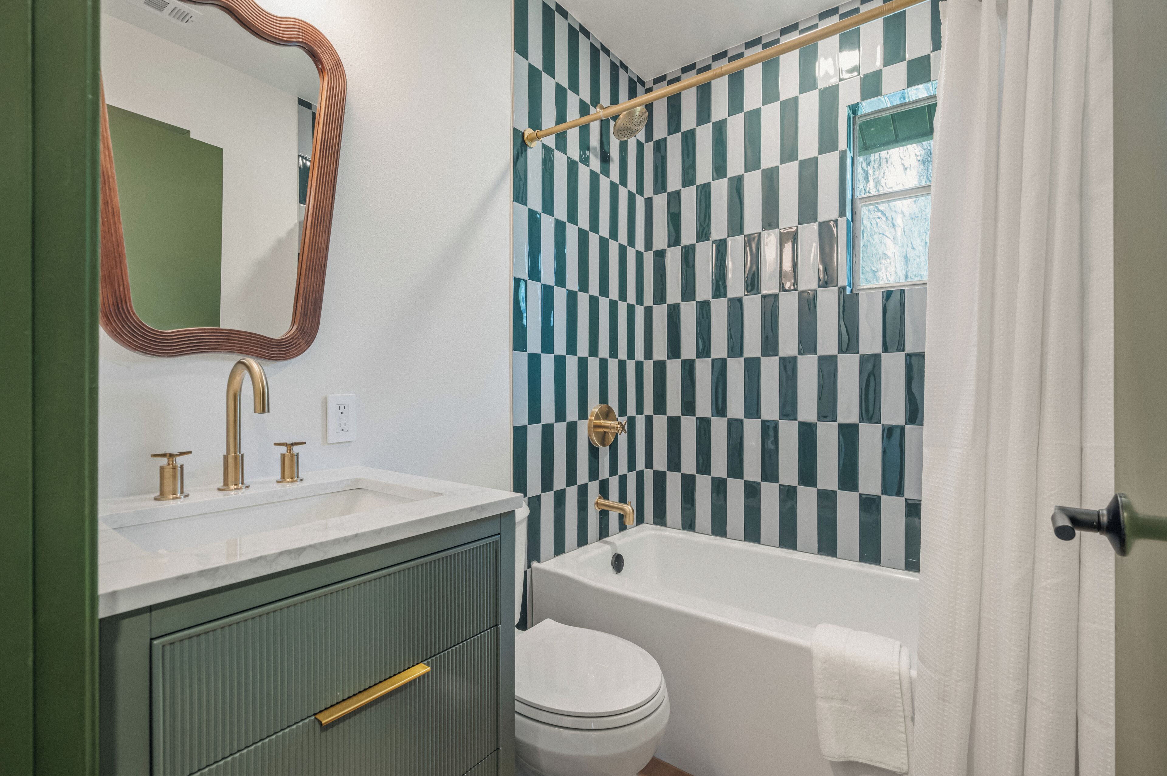 A bathroom with a checkered tile wall, a white bathtub, a white toilet, and a vanity with a mirror and gold fixtures.