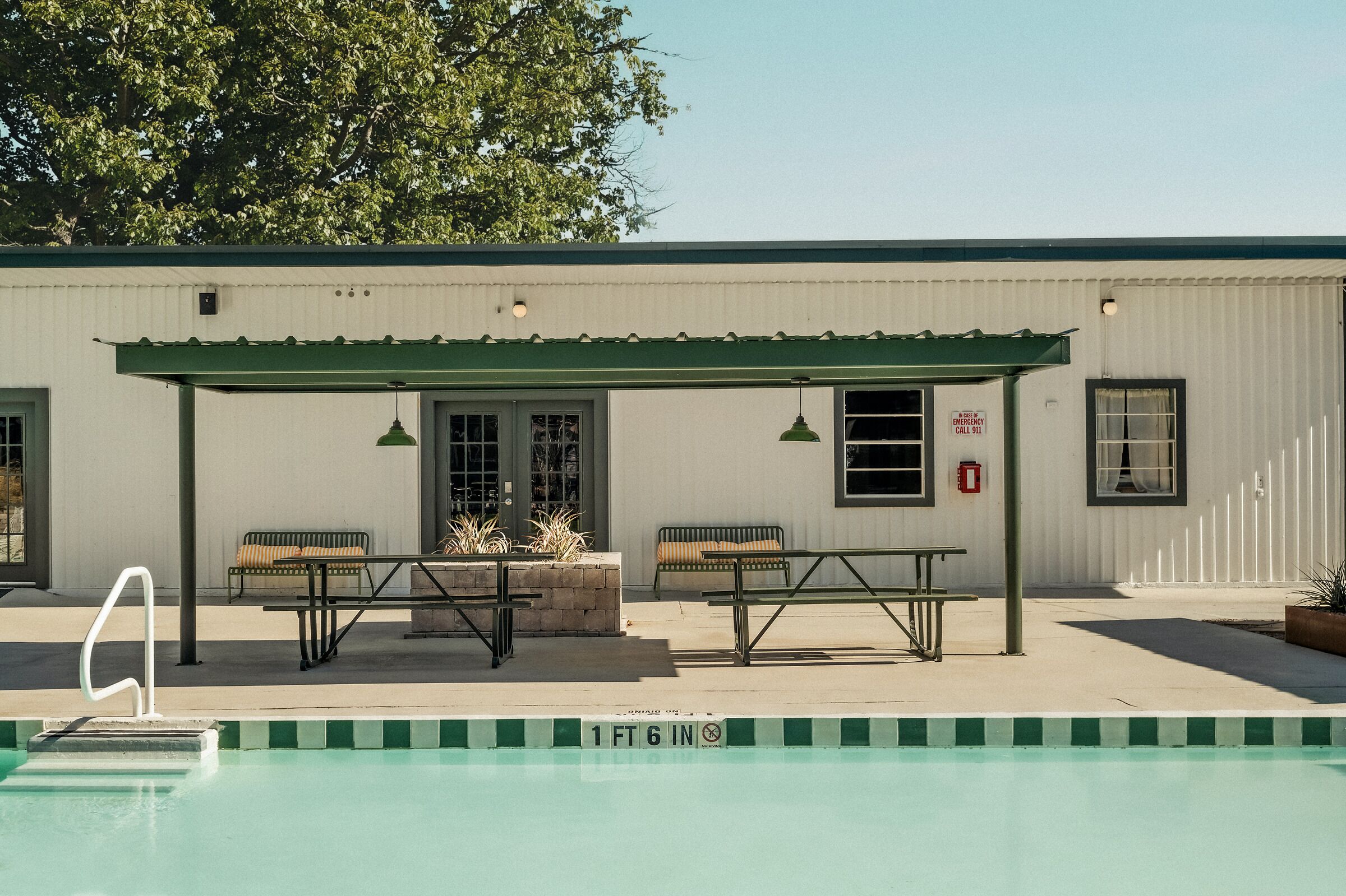 A pool area with a covered seating area, a table, and a bench.