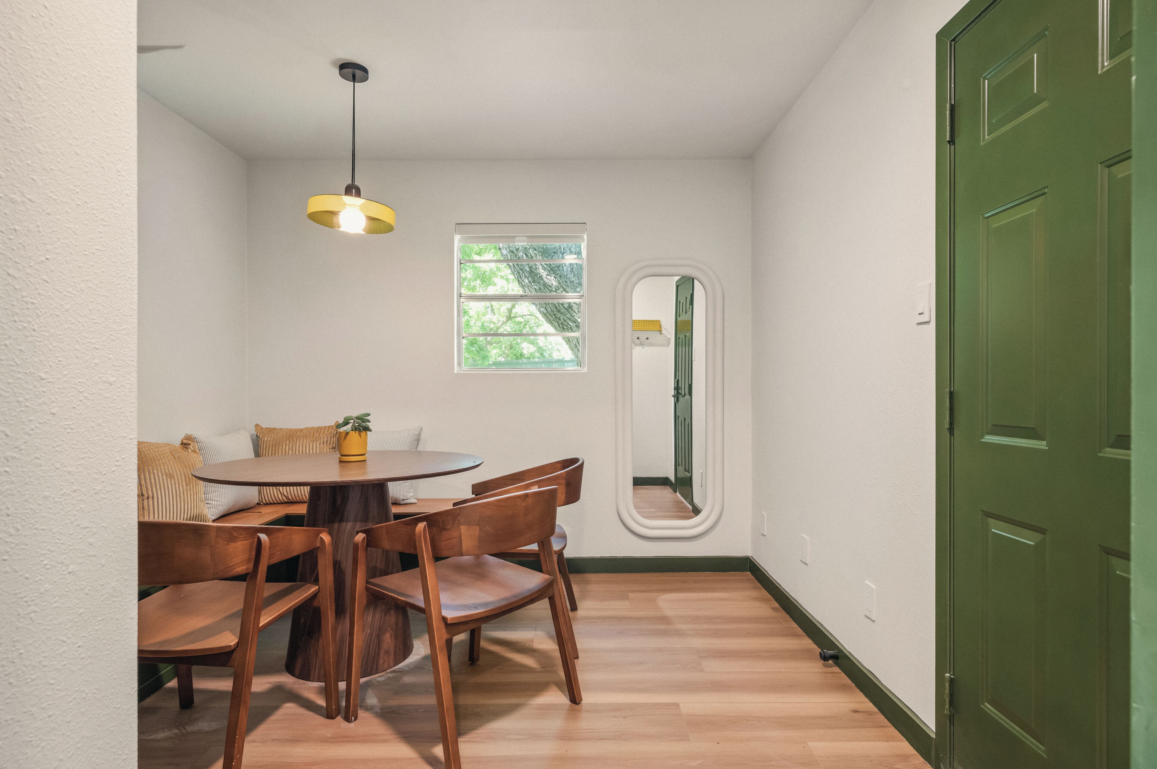 Un coin repas avec une table ronde, des chaises en bois, un luminaire suspendu, une fenêtre et une porte verte.