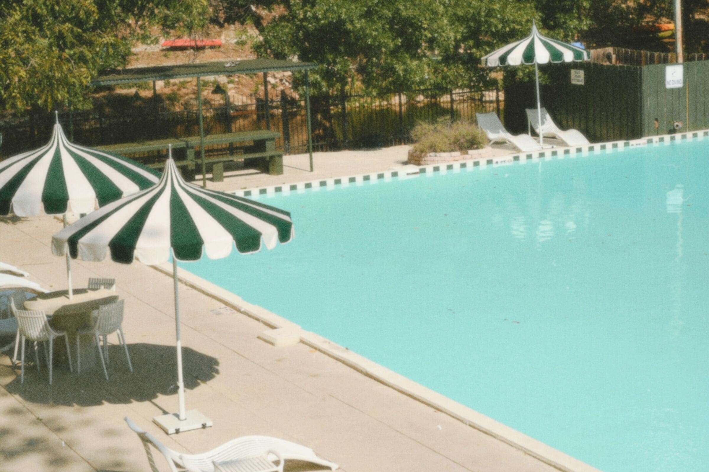 Una piscina con sillones de descanso y sombrillas a rayas.