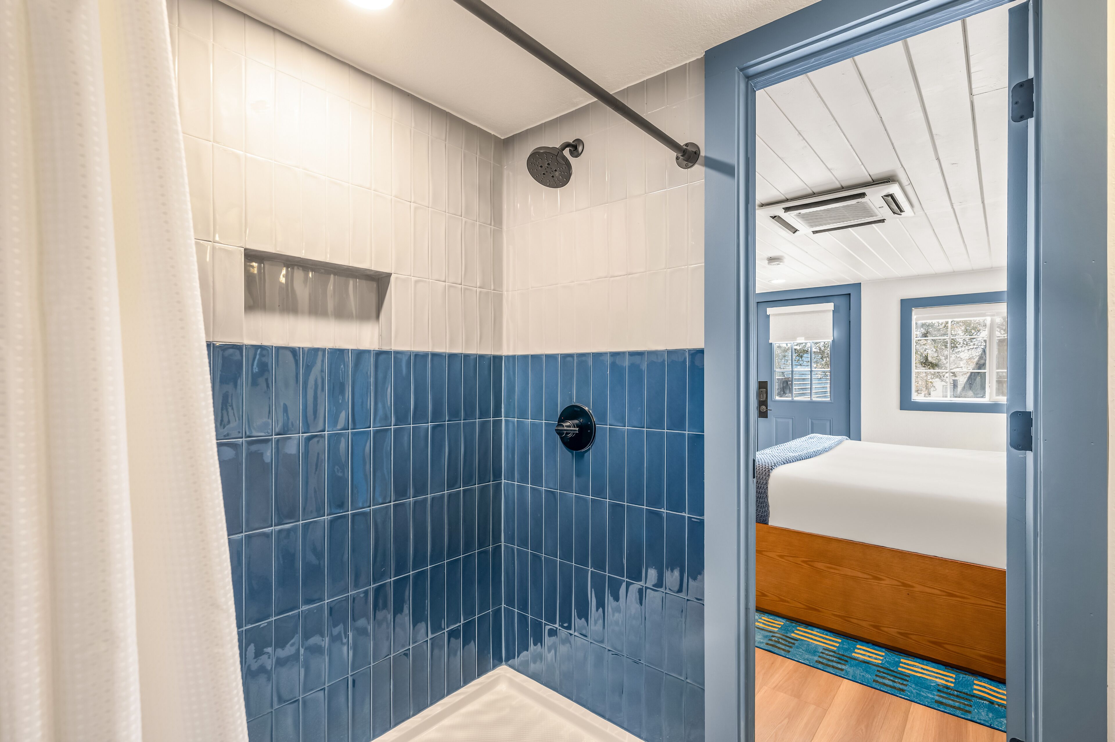 Un baño con azulejos azules, ducha y cama con cabecero de madera.