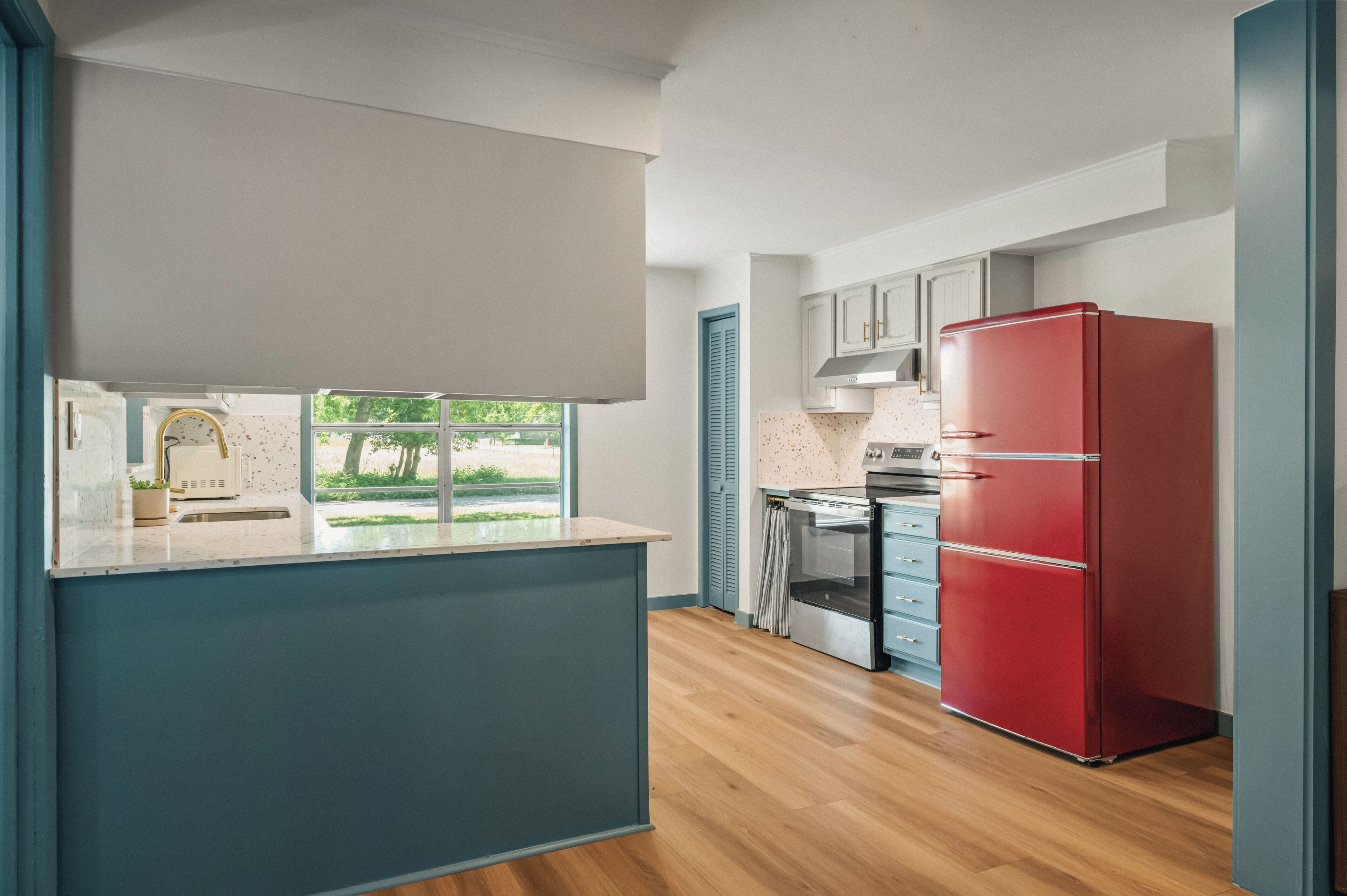 Une cuisine moderne avec un îlot central, un réfrigérateur rouge et une vue sur la verdure environnante.