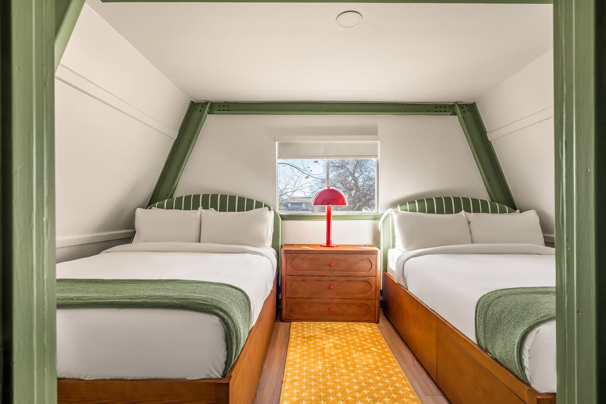 A bedroom with two beds, a window, a red lamp, and a patterned rug.