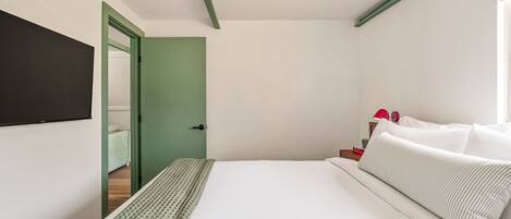 A modern hotel room with a bed, a green door, and a red lamp on a nightstand.