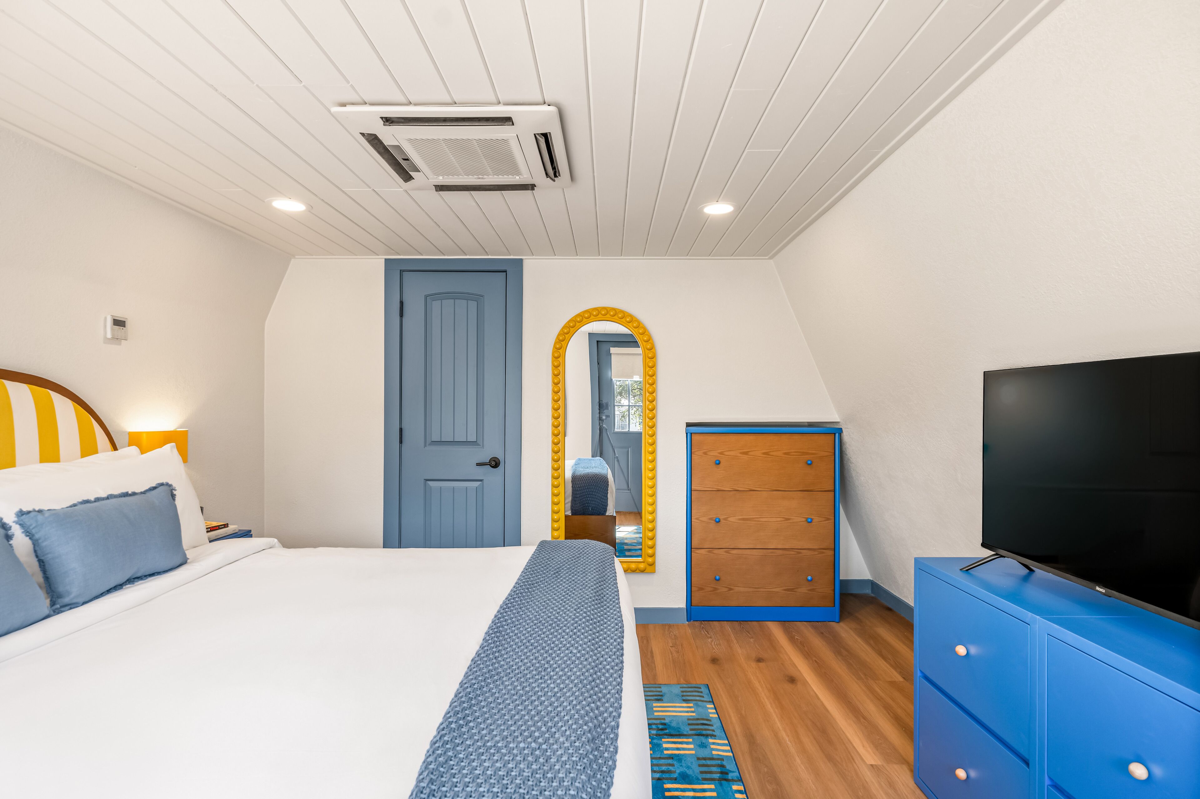 A bedroom with a bed, a dresser, a TV, a mirror, and a door.