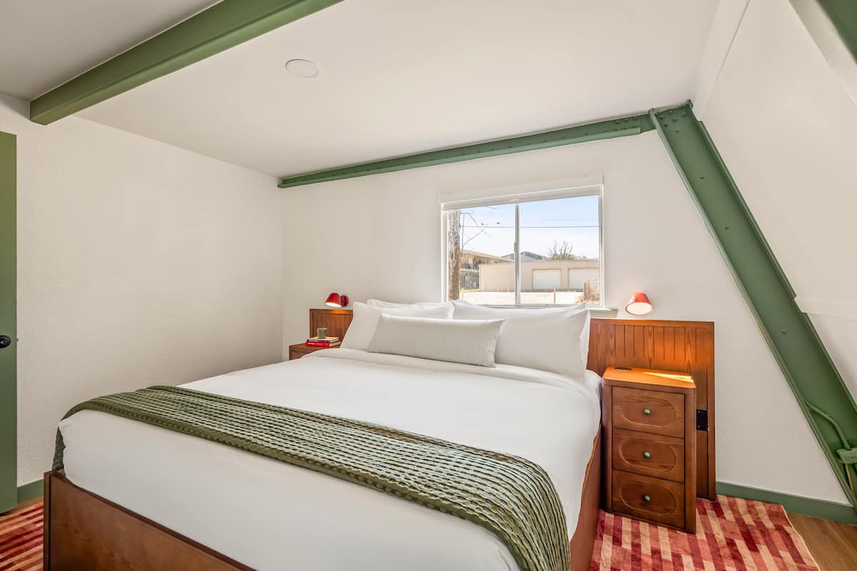 A bedroom with a bed, a window, a nightstand, and a lamp.