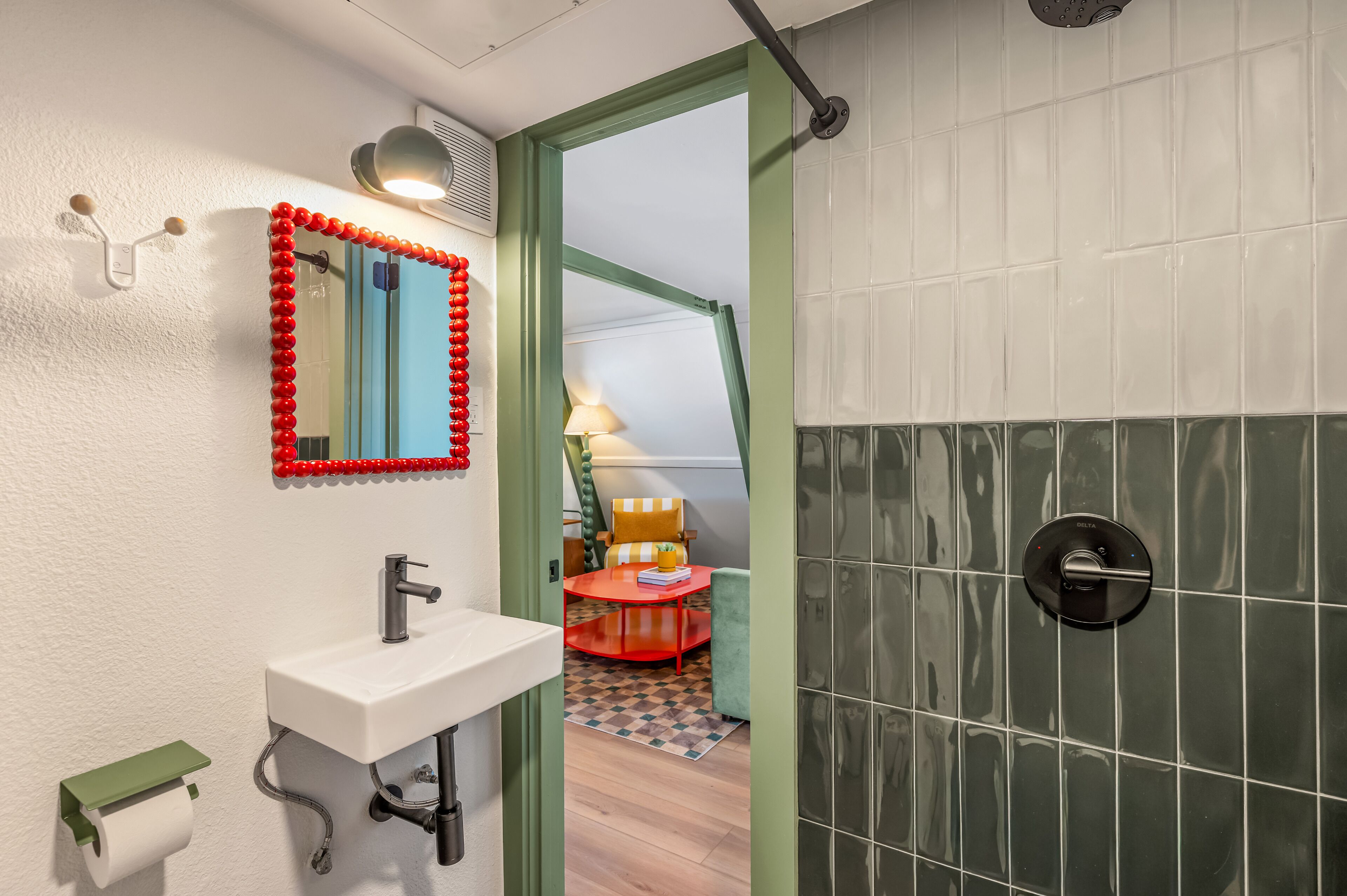 A bathroom with a white sink, a mirror with a red frame, and a shower area with green tiles.