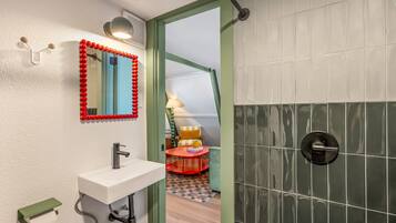 A bathroom with a white sink, a mirror with a red frame, and a shower area with green tiles.