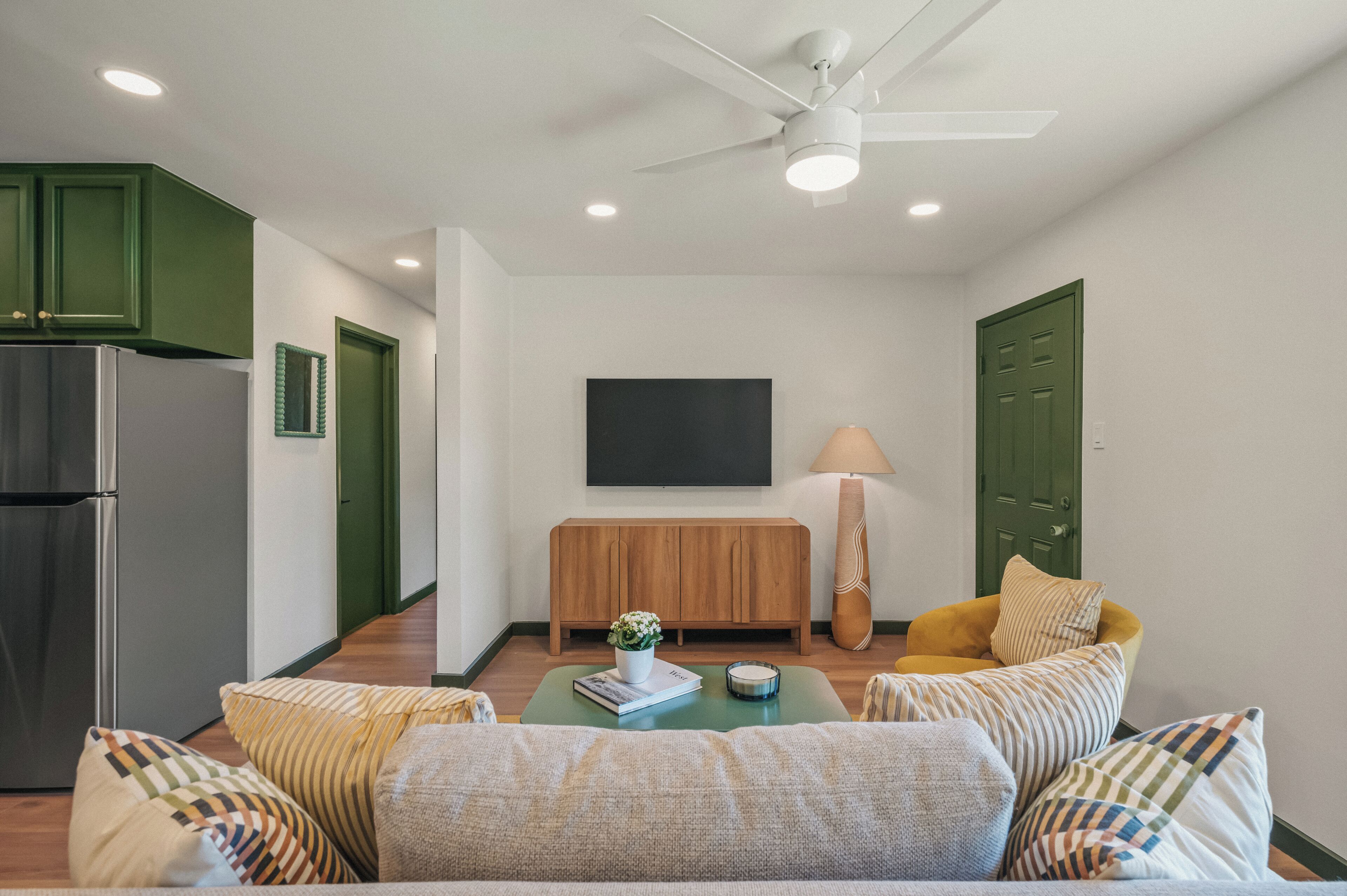 A compact living space with a kitchenette, a sofa set, a coffee table, a TV, and a lamp.