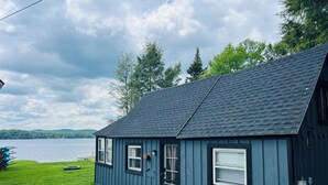 A blue house with a dark roof, a grassy yard, and a lake in the background.