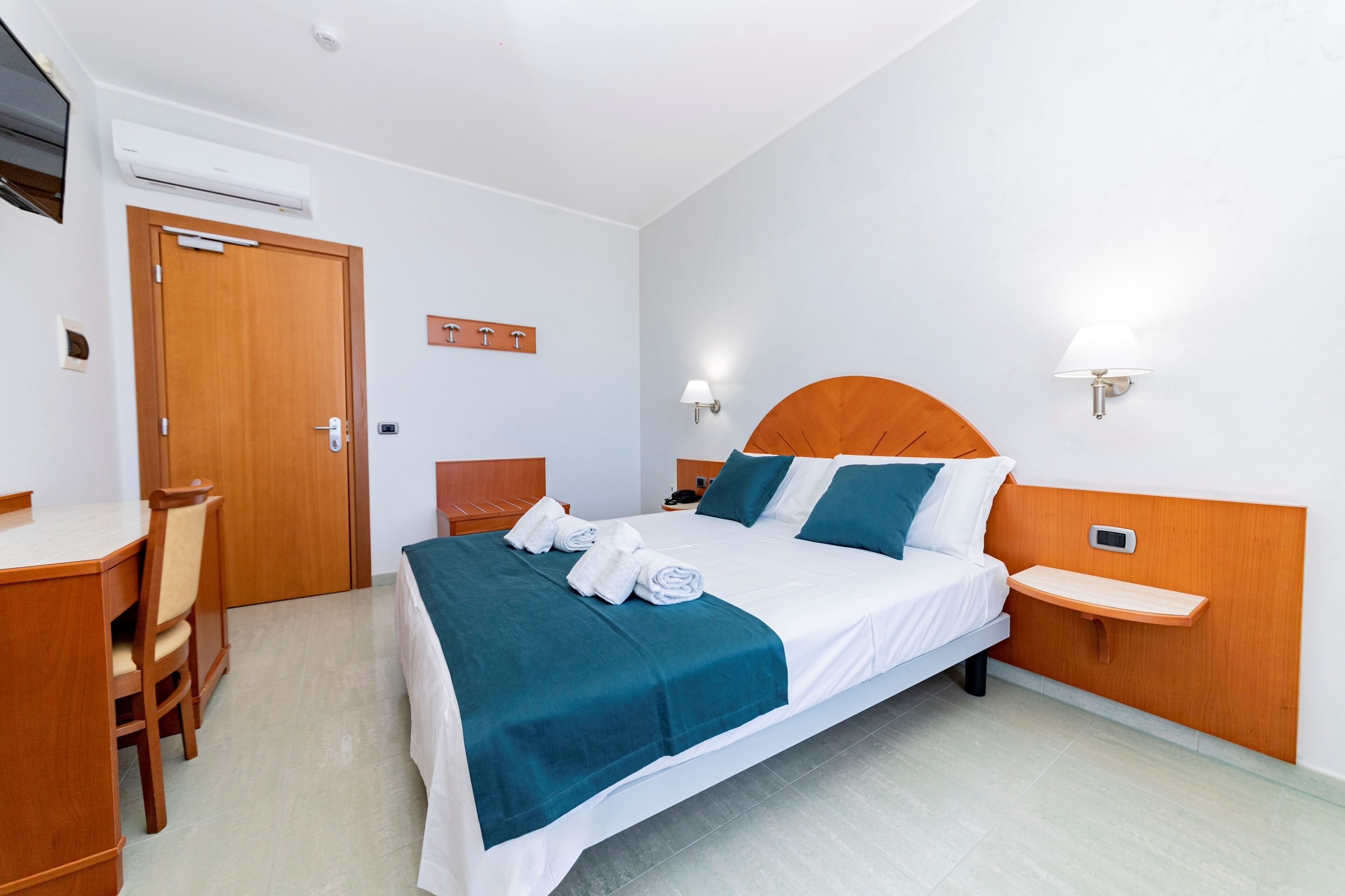 Ein Hotelzimmer mit Bett, Nachttisch, Lampe, Schreibtisch, Stuhl und Klimaanlage.