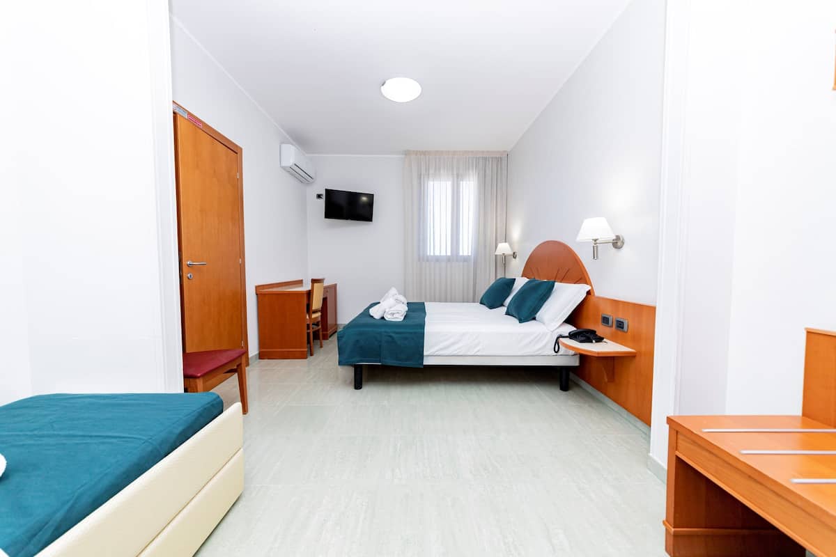A hotel room with a bed, a desk, a chair, a TV, and a window with curtains.