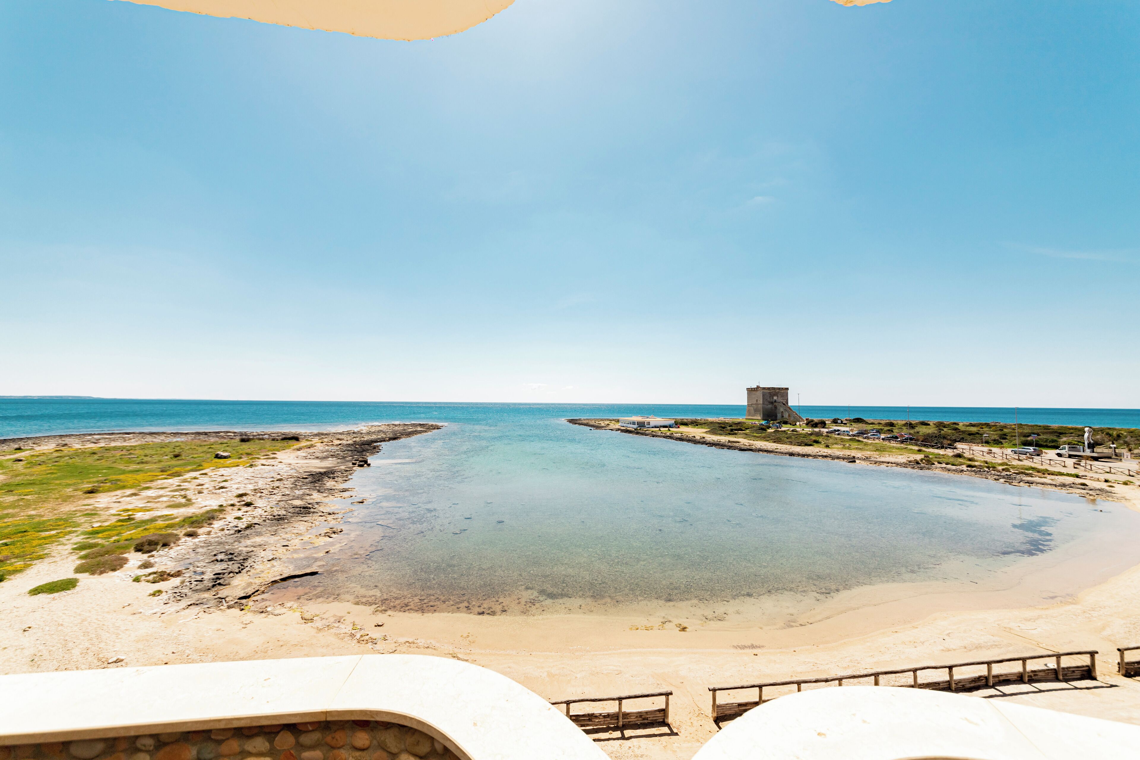 Blick auf die Küste, strahlend blauer Himmel, ein Sandstrand und ein kleiner Turm.