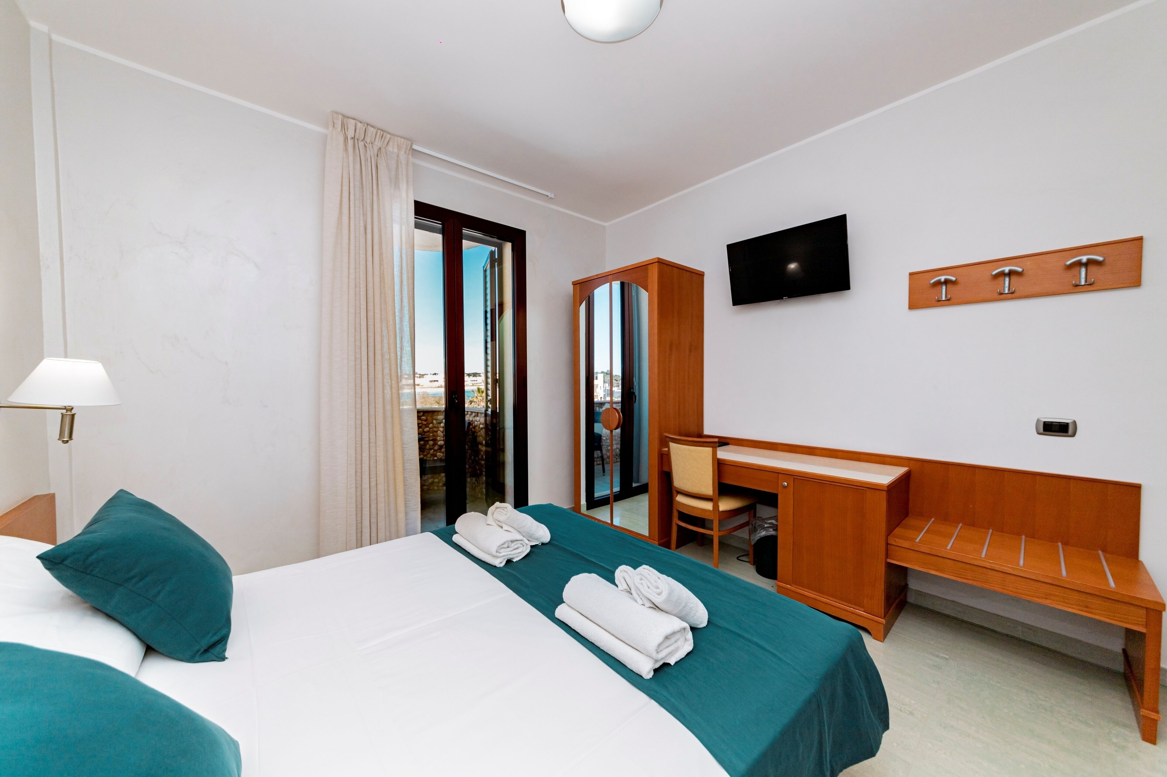 A hotel room with a bed, a desk, a chair, a TV, and a balcony with a view.