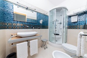 A modern bathroom with a glass-enclosed shower, a white sink, and a beige tiled wall. - Hotel Alba (Torre Lapillo)