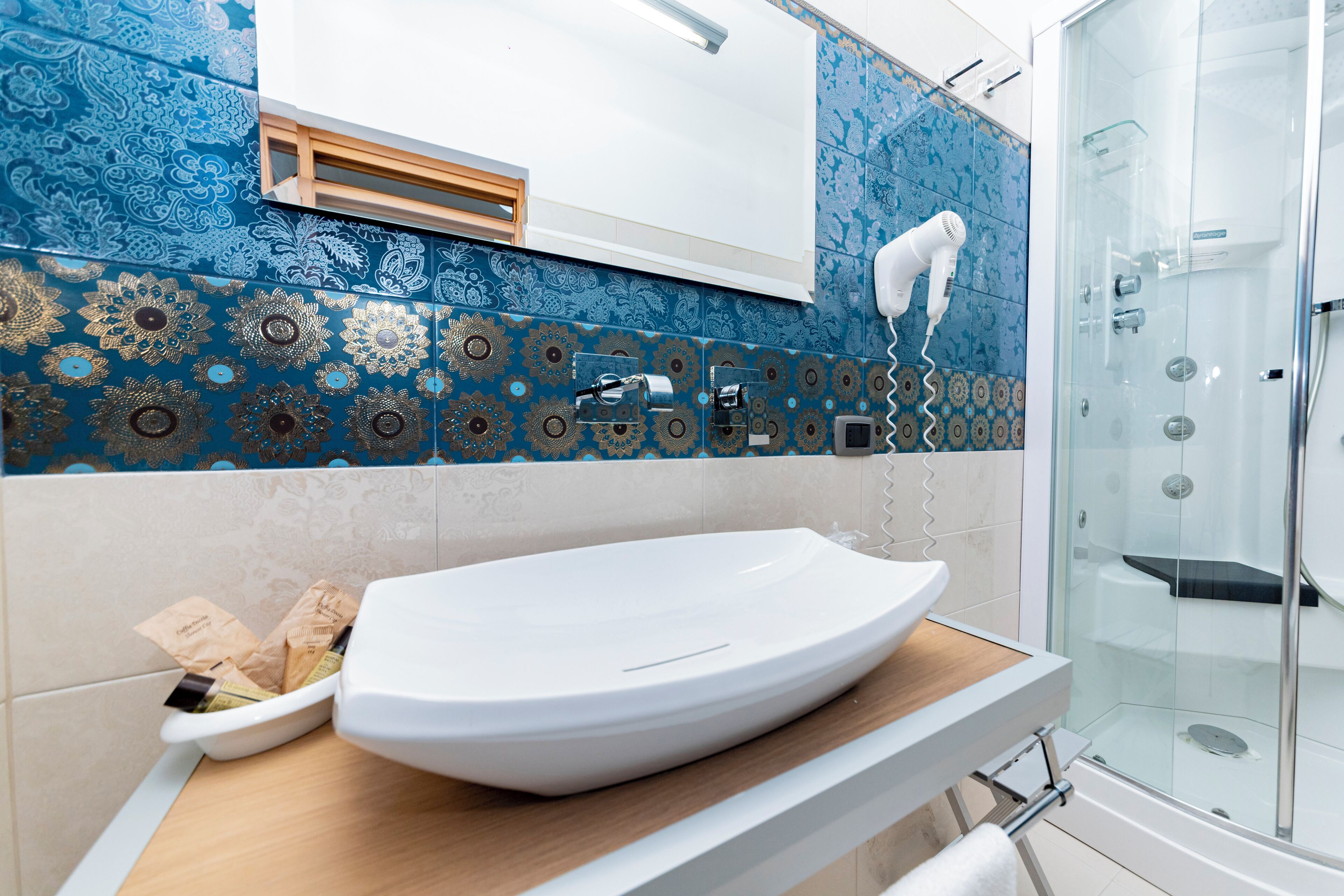 Een badkamer met een groot wit wastafelmeubel, een douchecabine van glas en betegelde wanden in blauw en beige.