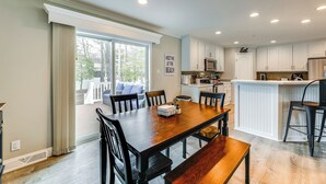 Una cocina moderna con armarios blancos, una isla central y una zona de comedor con una mesa y sillas de madera.