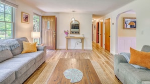 A living room with a sofa, a coffee table, and a hallway leading to a door. - Classic Cape Cod Escape: Beaches and Backyard BBQs (Wellfleet)