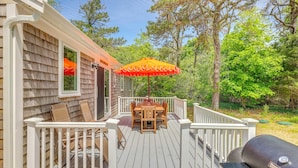 A deck with a table and chairs, a barbecue grill, and a white railing. - Classic Cape Cod Escape: Beaches and Backyard BBQs (Wellfleet)