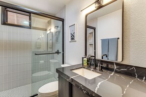 A modern bathroom with a glass shower enclosure, a white toilet, a marble sink, and a large mirror. - Sledding Thrills & Fireside Warmth: Pinetop Home (Pinetop)