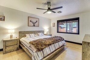 A bedroom with a wooden bed, two bedside tables, a ceiling fan, and a window with a view of a house. - Sledding Thrills & Fireside Warmth: Pinetop Home (Pinetop)