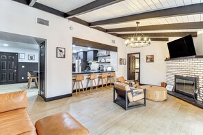 A spacious living area with a fireplace, a kitchen in the background, and a bar area with stools. - Sledding Thrills & Fireside Warmth: Pinetop Home (Pinetop)