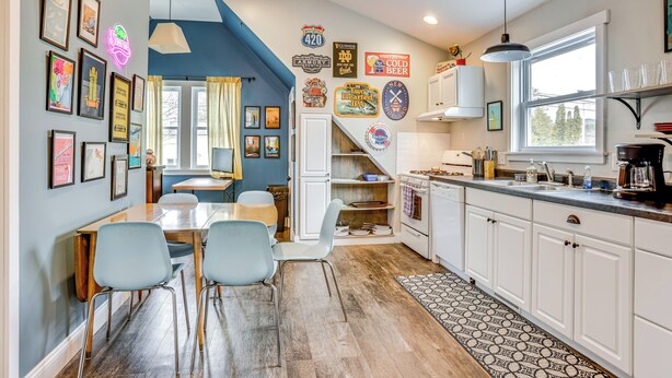 A kitchen with white cabinets, a dining area with a table and chairs, and various wall decorations including framed pictures and neon signs. - Close to Trails & Town! Artsy Apt in Frankfort (Frankfort)