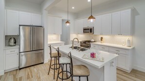 A modern kitchen with white cabinetry, stainless steel appliances, and a central island with bar stools.