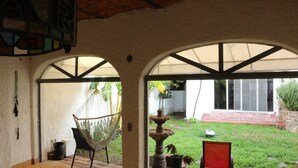 A covered patio area with a hammock chair, a small fountain, and a view of a garden with a white wall and steps. - Room-your Best Hideaway in the Coolest n (Zapopan)