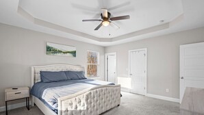 Une chambre à coucher avec un lit doté d’une tête de lit capitonnée, un ventilateur de plafond et une fenêtre avec des stores.