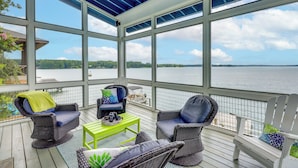 Eine überdachte Terrasse im Freien mit Korbmöbeln, einem grünen Tisch und Blick auf das Wasser.