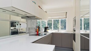 Een moderne keuken met witte aanrechtbladen, roestvrijstalen apparatuur en een groot raam voor natuurlijk licht.