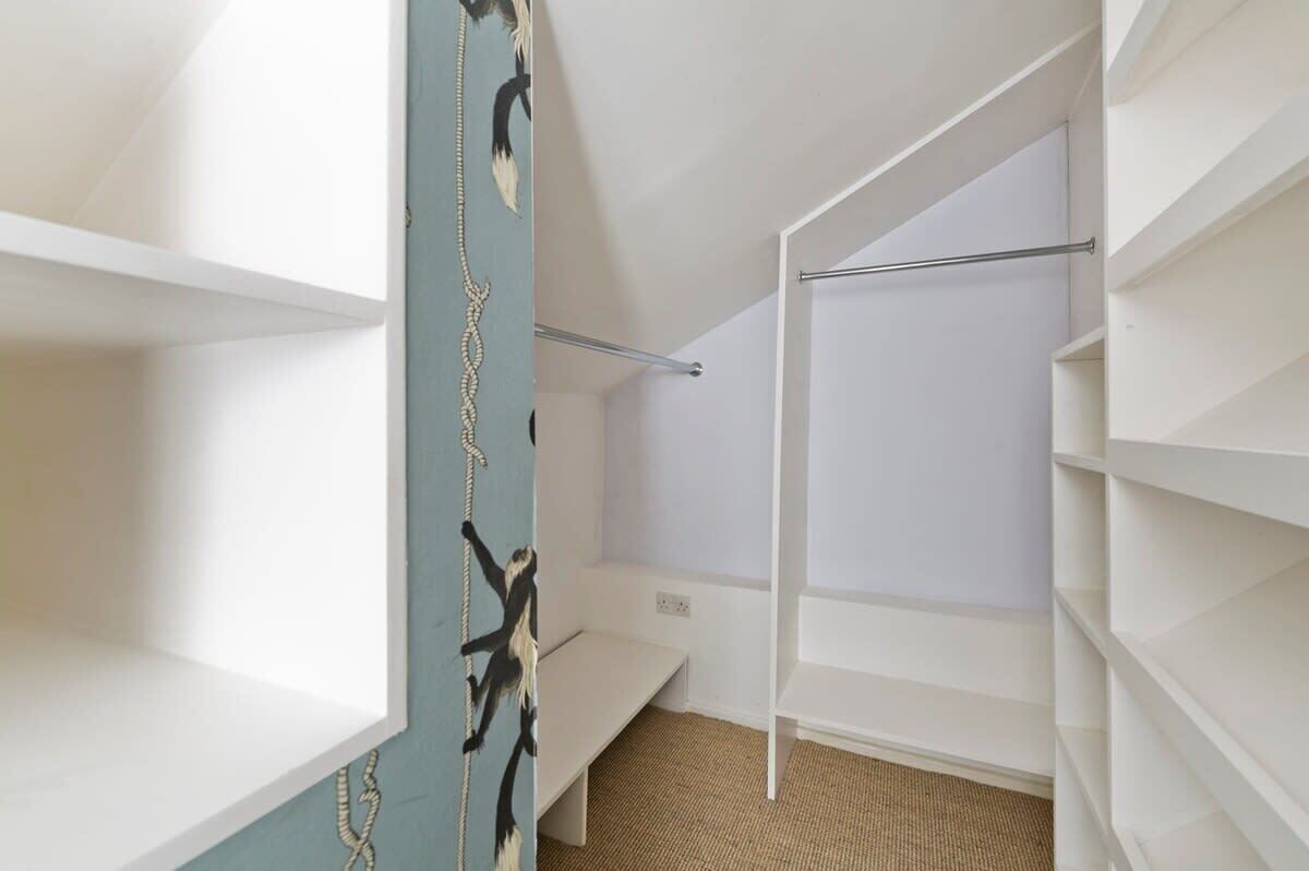 A walk-in closet with white shelves, a bench, and a hanging rod.