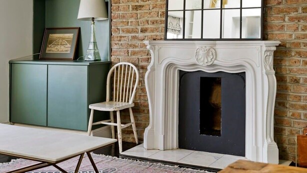 A room with a brick wall, a white fireplace, a green cabinet, and a chair. - 1 Bed Bohemian Loft Style Apt (London)