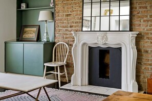 A room with a brick wall, a white fireplace, a green cabinet, and a chair.