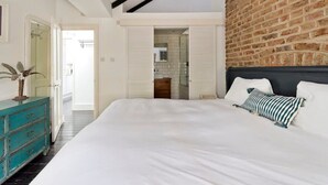 A bedroom with a large bed, a wooden headboard, a teal dresser, and a brick wall. - 1 Bed Bohemian Loft Style Apt (London)