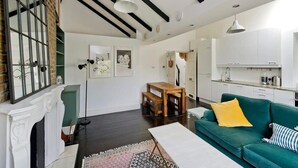 A modern living room with a green sofa, a wooden coffee table, and a fireplace. There is a kitchen area with white cabinets and a dining table. - 1 Bed Bohemian Loft Style Apt (London)