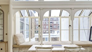 A room with a bay window, a cushioned bench, a table with chairs, and a view of buildings outside. - Grand 2 Bedroom Flat, Kensington (London)