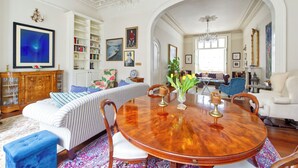 A spacious living room with a round wooden dining table, a striped sofa, and a bookshelf. - Grand 2 Bedroom Flat, Kensington (London)