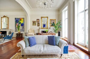 Ein geräumiges Wohnzimmer mit einem gestreiften Sofa, einer Chandelüster und großen Fenstern.