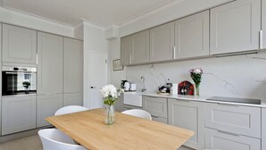 A modern kitchen with white cabinets, a wooden table, and white chairs. - Large & Wonderful 1 Bed, Pimlico (London)