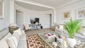A modern living room with a sofa, coffee table, and a television. There is a plant on the coffee table and a patterned rug on the floor. - Large 1 Bedroom Apartment - Chelsea (London)
