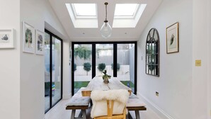 A dining area with a high ceiling, skylights, and a view of a garden through large glass doors. - Central London 4BR Queens Park Family Home With Garden (London)